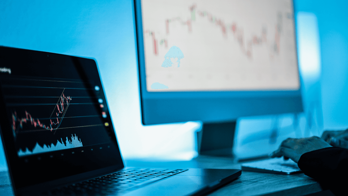 There are two computer screens that display stock charts